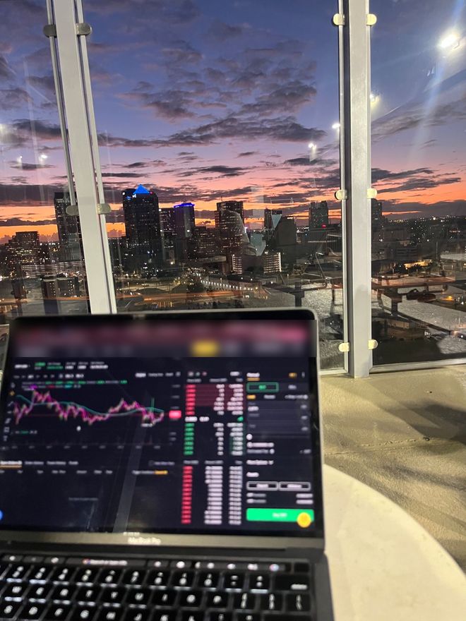 Laptop with charts open, city skyline at dusk behind it